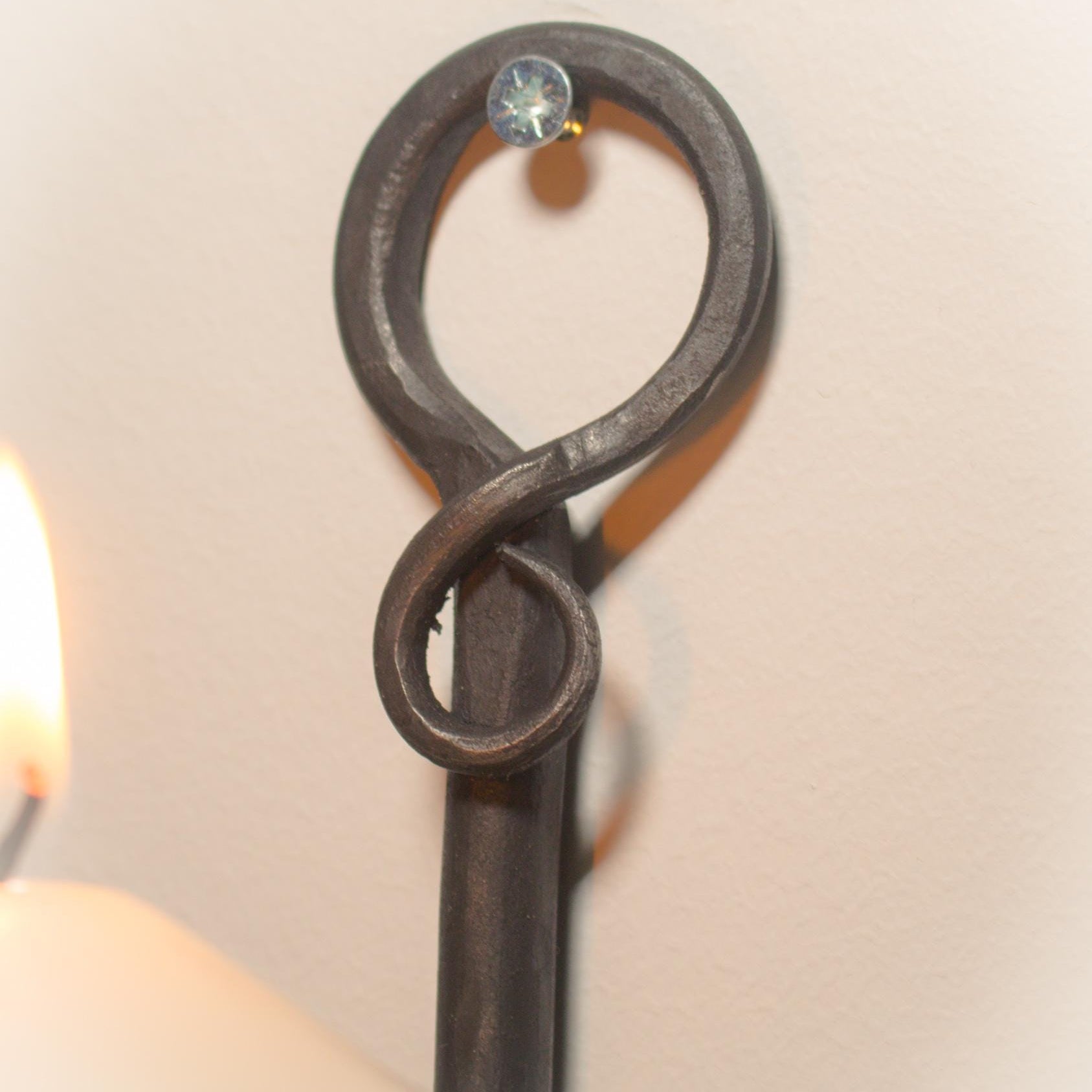 Rustic wall candle sconce crafted from hand-forged iron, holding a lit candle.