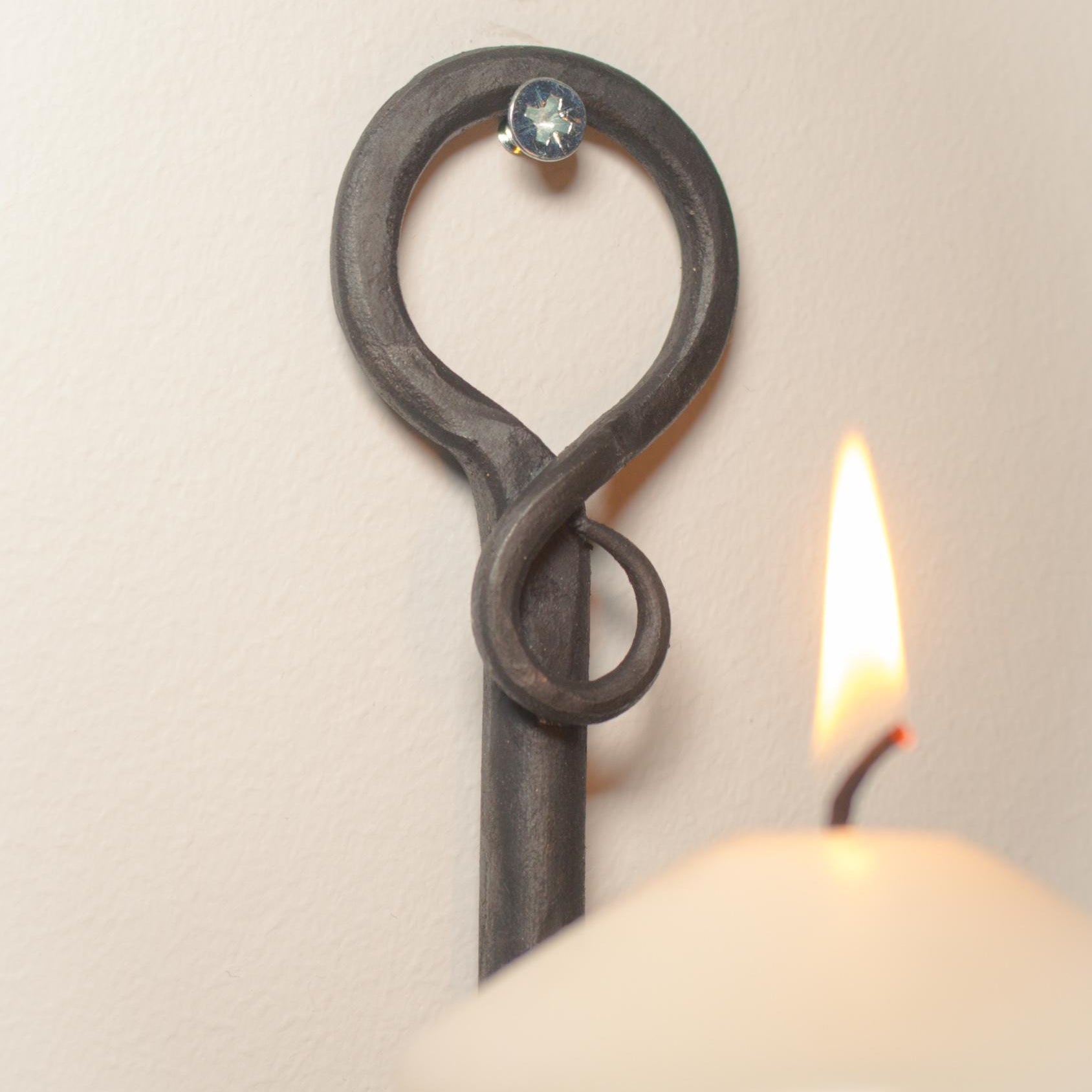 Side view of a hand-forged metal candle holder with a glowing white pillar candle.