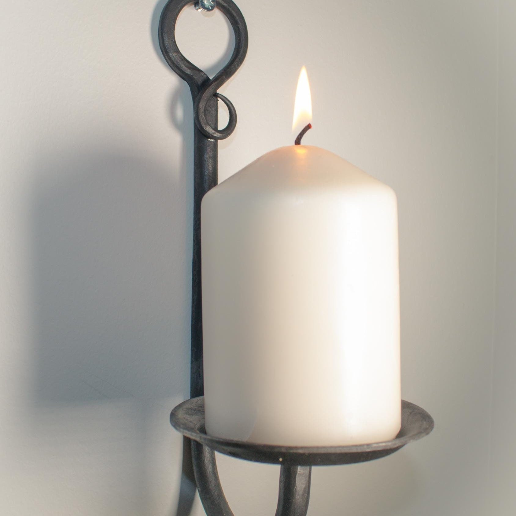 Hand-forged rustic wall candle holder with a gem accent and a lit white pillar candle.