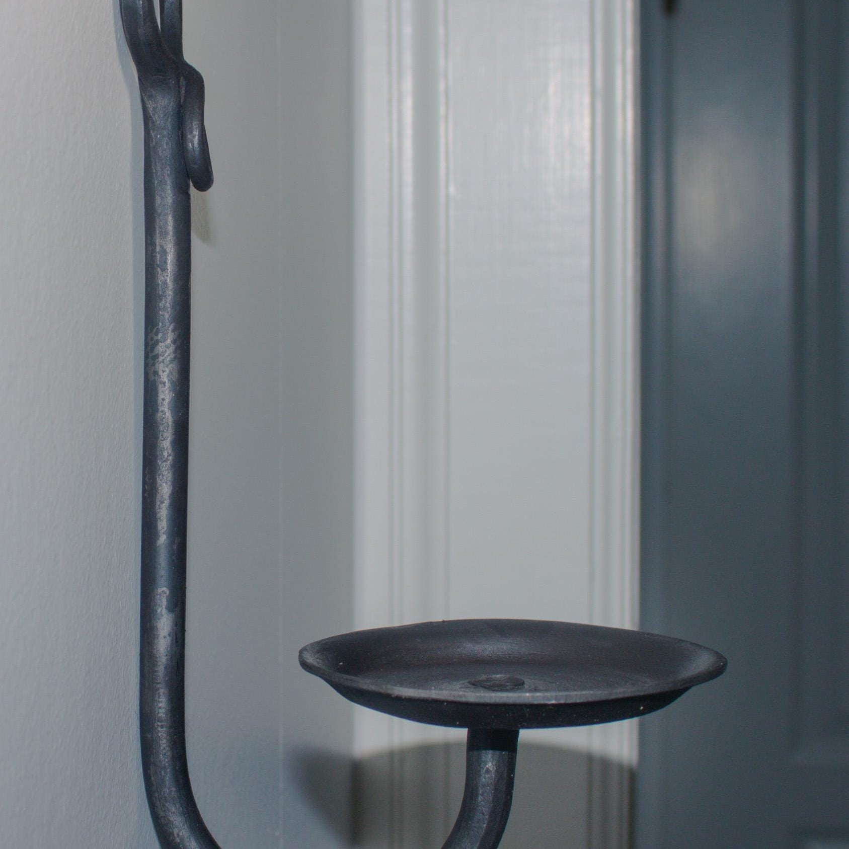 Close-up of a blacksmith-crafted iron candle holder mounted on a wall.