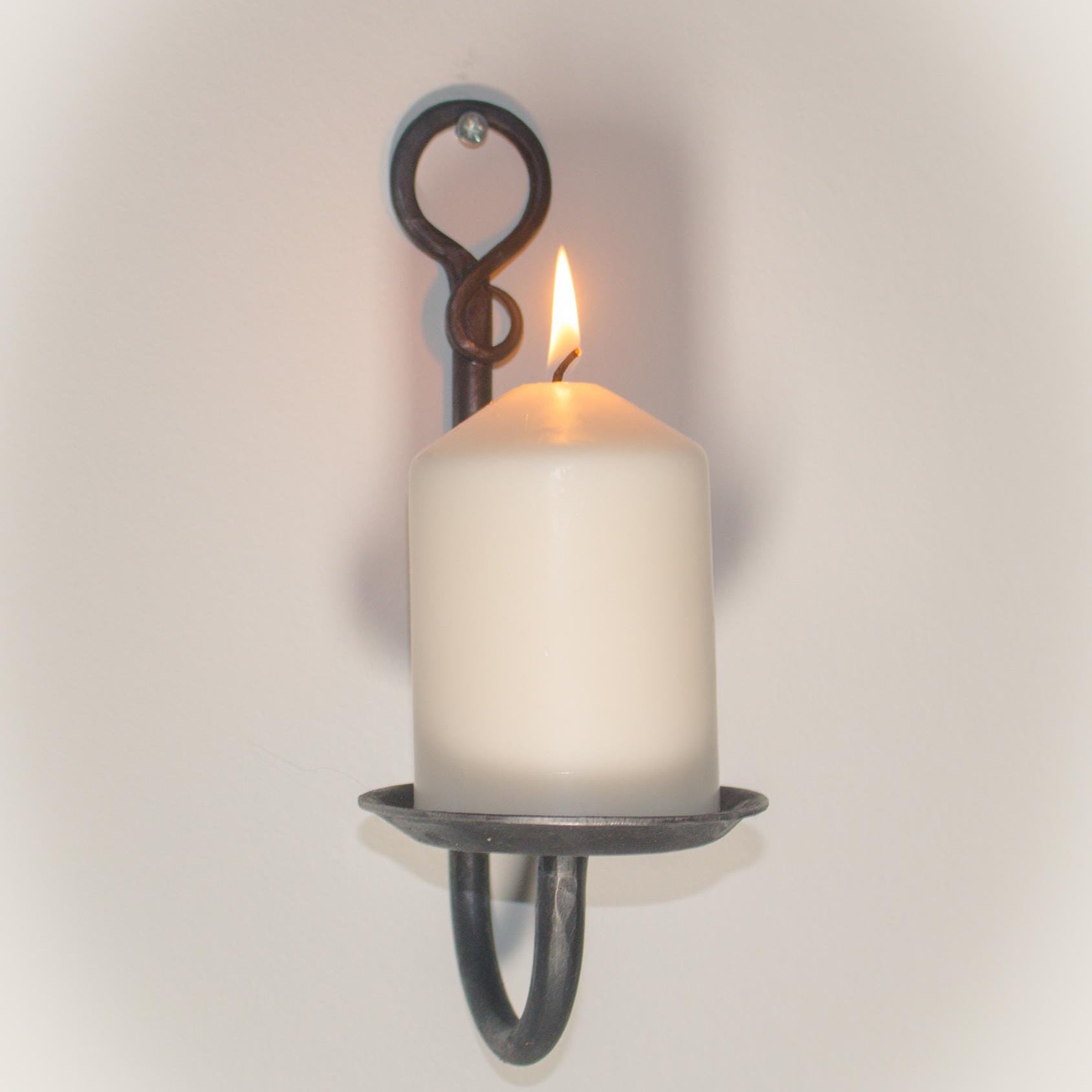 Rustic iron wall sconce holding a white candle, perfect for home decor.