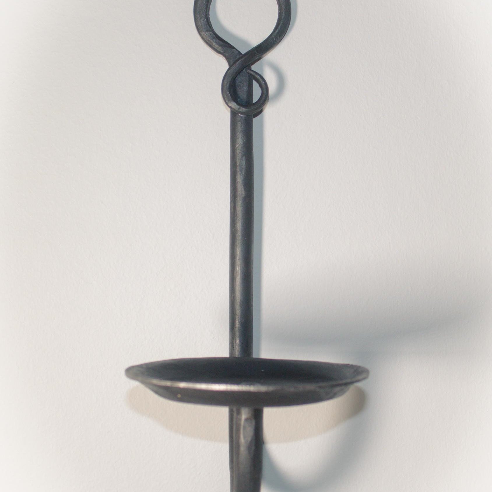 Medieval-inspired blacksmith candle sconce mounted on a white wall.