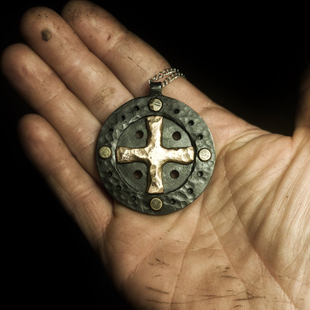 a hand holding sun cross pendant that is made out of iron and bronze