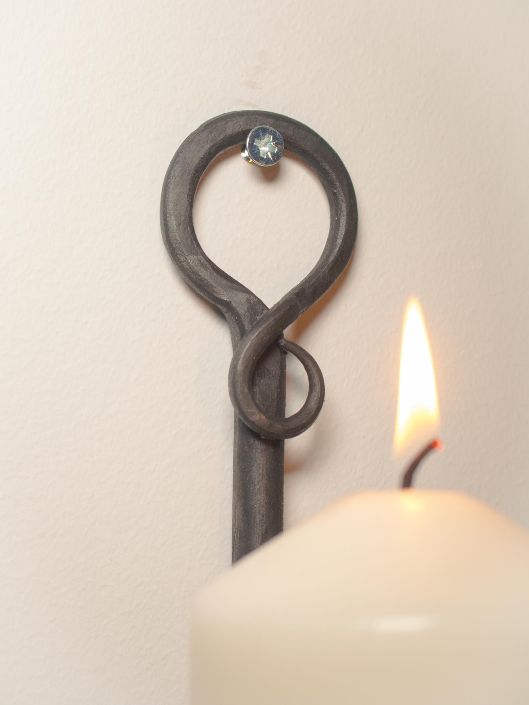 Side view of a hand-forged metal candle holder with a glowing white pillar candle.