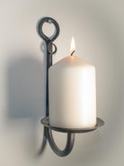 Hand-forged rustic wall candle holder with a gem accent and a lit white pillar candle.