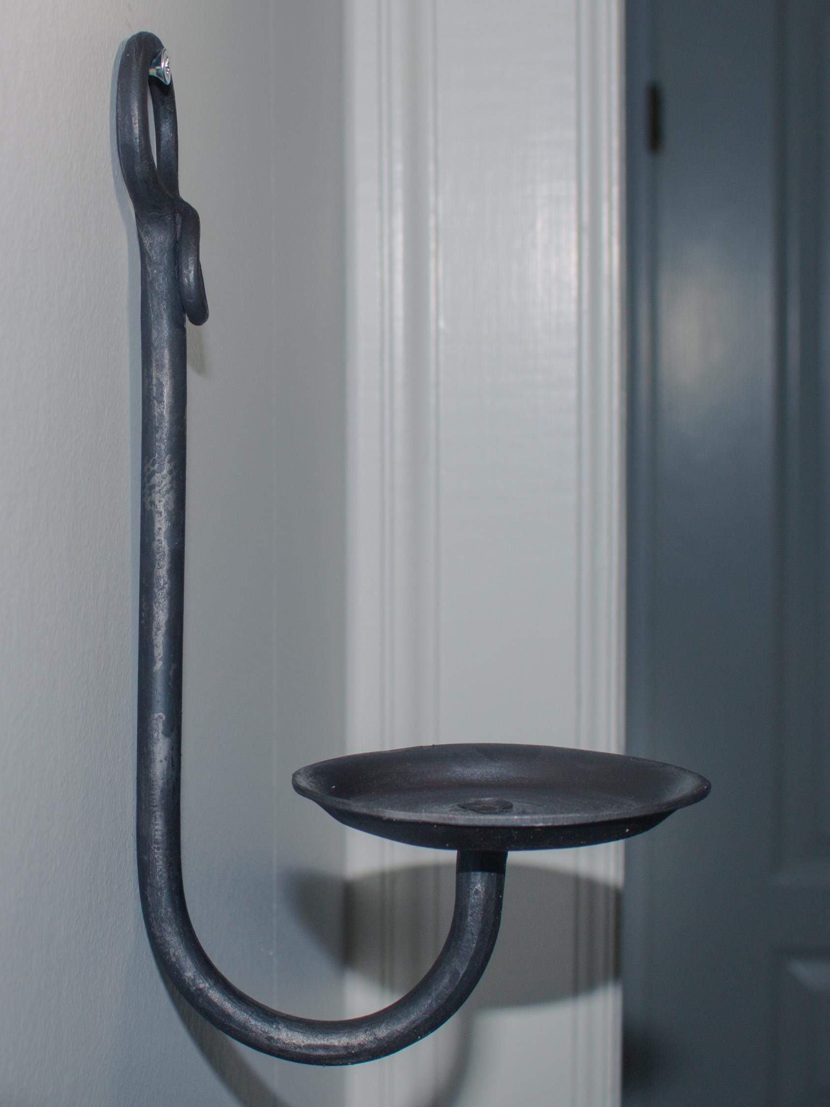 Close-up of a blacksmith-crafted iron candle holder mounted on a wall.