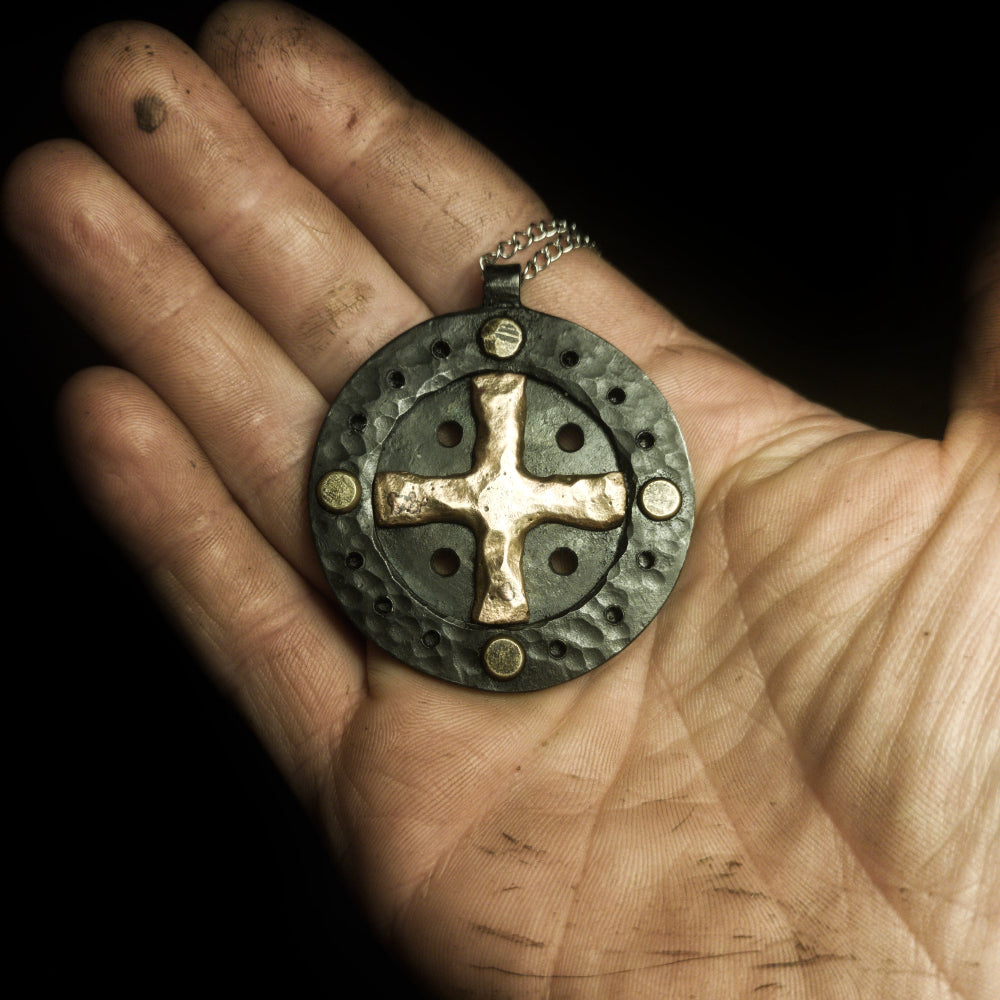 a hand holding  sun cross pendant that is made out of iron and bronze