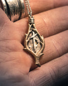 Close-up macro shot of a bronze Viking amulet with combined runes, suspended on a silver chain against a black surface